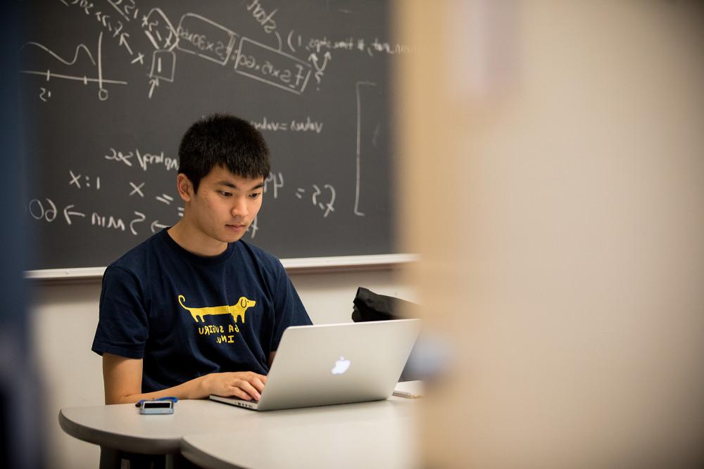 A student studies in a classroom, mathematical equations scrawled on the chalkboard behind them.