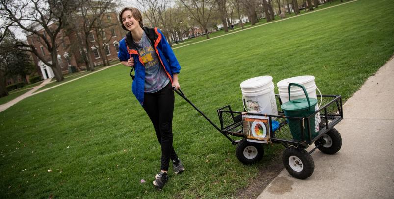 Jennifer Pantelios的19岁学生在校园里用堆肥车收集食物残渣. 她给出...
